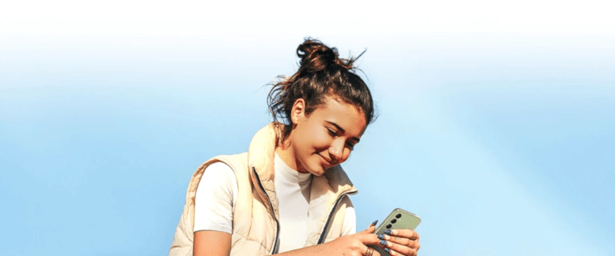 zdjęcie firmy Samsung młodej uśmiechniętej kobiety trzymającej smartfona z potrójnym aparatem fotograficznym