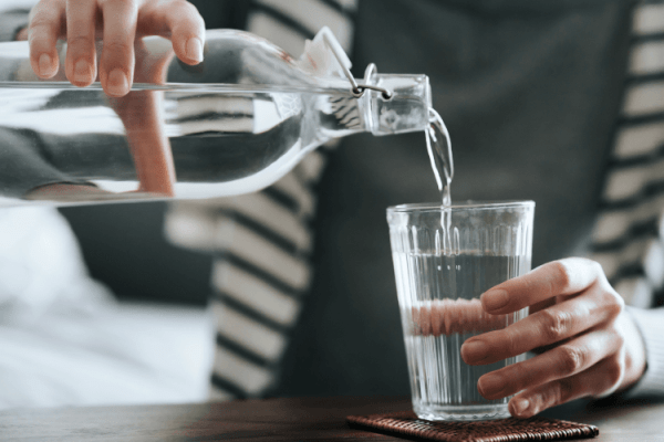 zdjęcie przedstawiające osobę nalewającą wodę z butelki do szklanki