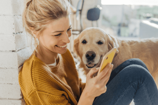 zdjęcie przedstawiające psa rady golden i siedzącą młodą kobietę w blond włosach śmiejącą się do smartfona