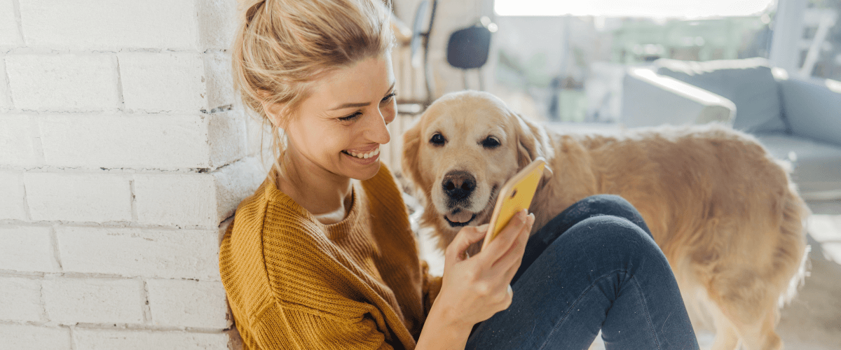 zdjęcie przedstawiające psa rady golden i siedzącą młodą kobietę w blond włosach śmiejącą się do smartfona