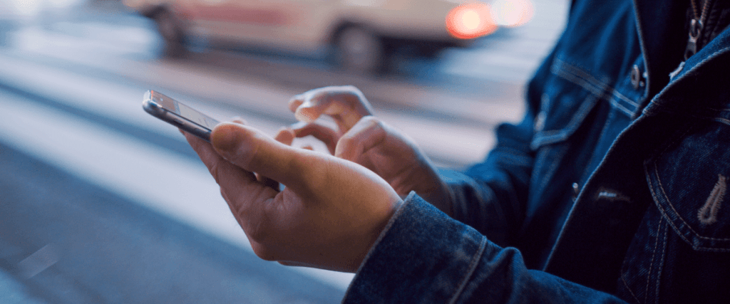 zdjęcie przedstawiające w przybliżeniu mężczyznę na ulicy klikającego w ekran dotykowego smartfona