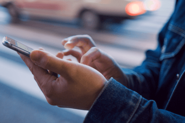 zdjęcie przedstawiające w przybliżeniu mężczyznę na ulicy klikającego w ekran dotykowego smartfona