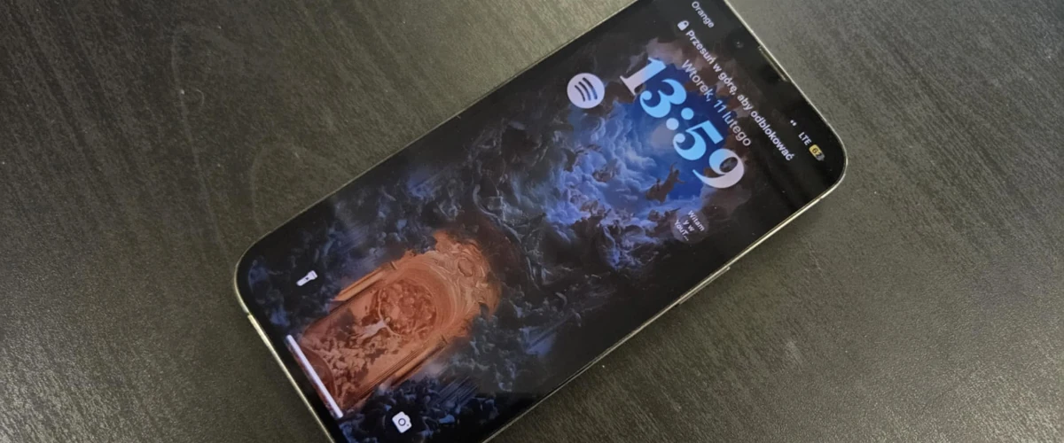 zdjęcie przedstawiające iPhone'a z włączonym ekranem leżącego na ciemnym biurku