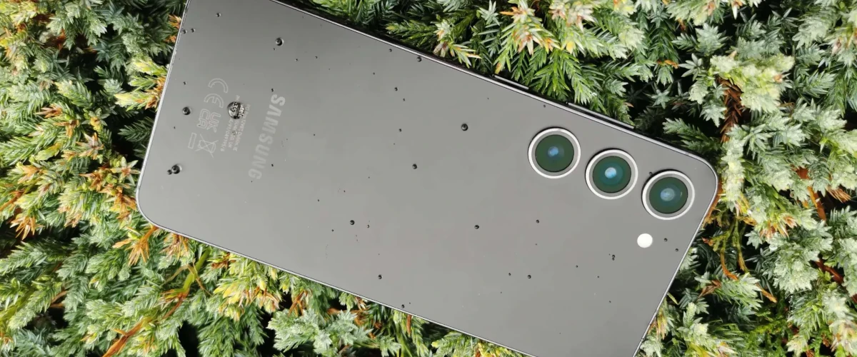 zdjęcie przedstawiające smartfona Samsung Galaxy S23 w czarnym kolorze leżącym na ekranie na zielonych gałązkach